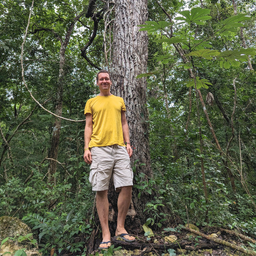 Marek steht lächelnd vor einem Breiapfelbaum im Dschungel.